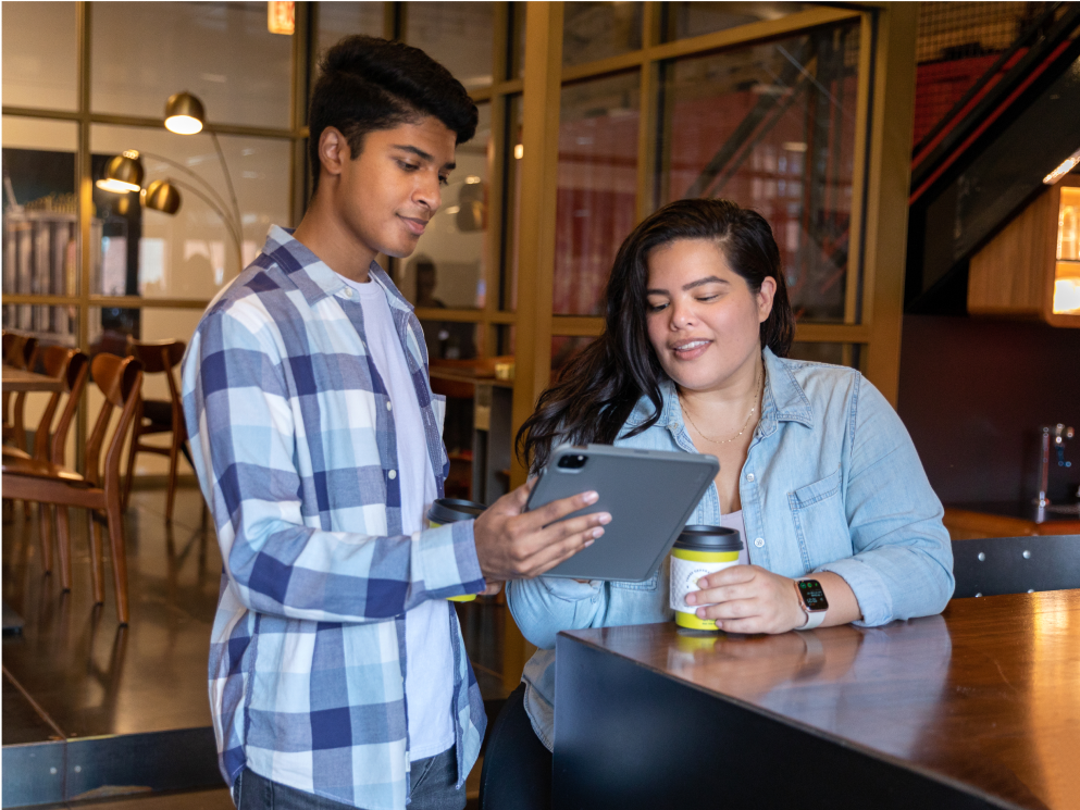 Two Sprout employees work on a shared tablet in a coffee shop.