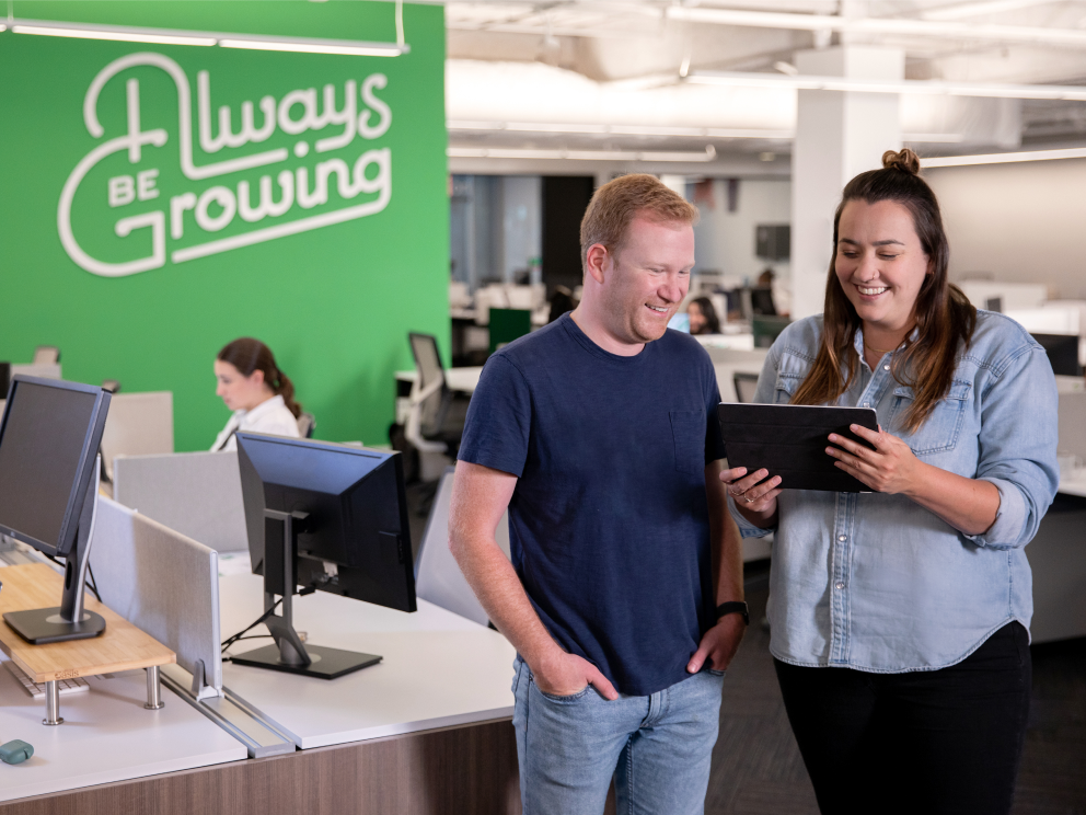 Two team members reviewing a contract together in front of our Always Be Growing in-office mural. 