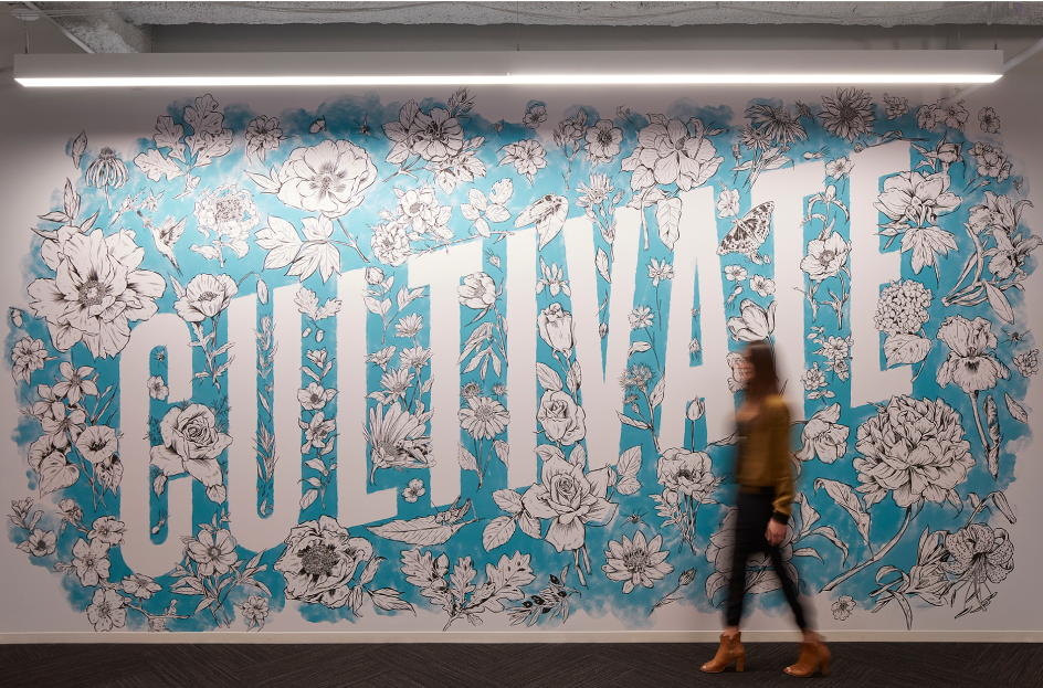 A mural covering an office wall with illustrated flowers surrounding the word “Cultivate” on a bright blue background.
